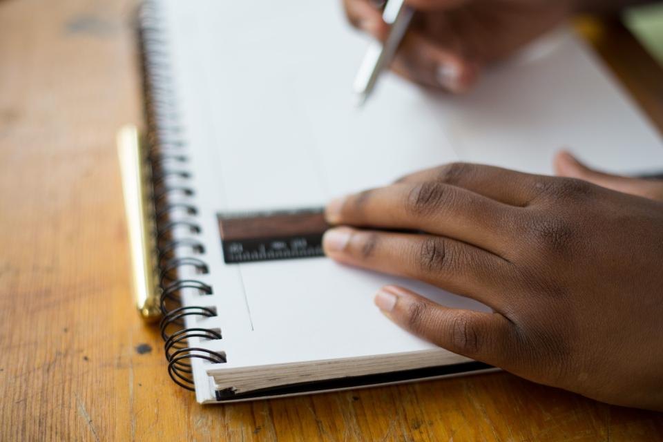 Main d'élève tenant une règle et un stylo sur un cahier à spirale, illustration du calcul de moyenne scolaire