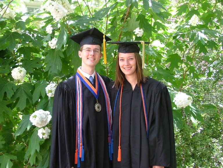 Deux jeunes diplômés en toge souriants dans un jardin, pour calculer sa moyenne au brevet, au bac et en BTS