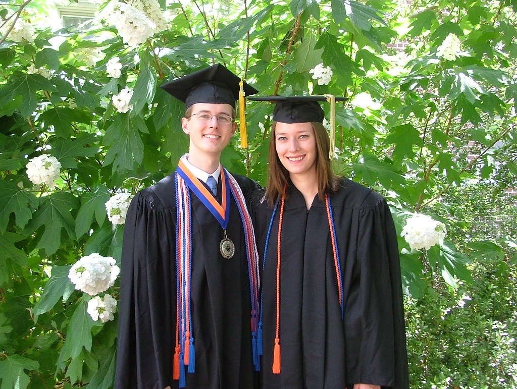 Deux jeunes diplômés en toge souriants dans un jardin, pour calculer sa moyenne au brevet, au bac et en BTS